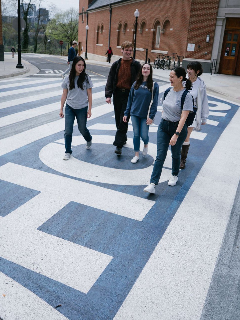 Five students walk across the street on a crosswalk that says HOYAS.